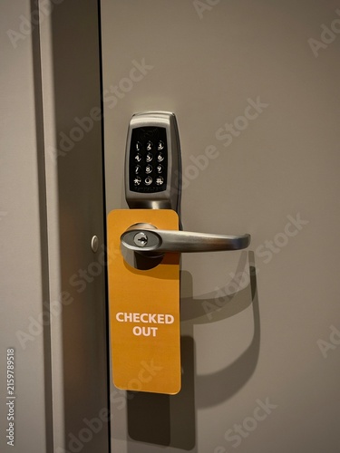 Reykjavik, Iceland - May 09, 2026: Door handle with digital keypad lock and yellow checked out sign hanging on a gray door in a modern hotel setting
