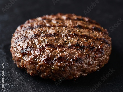 Juicy seasoned beef burger patty with charred grill marks cooking on a hot cast-iron pan