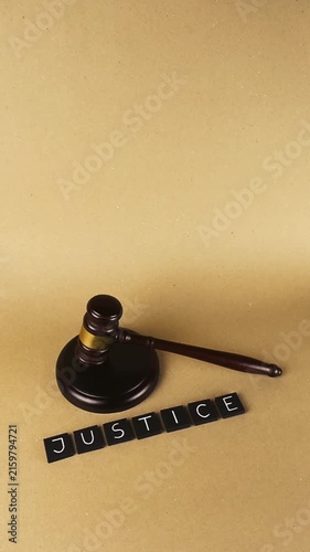 Wooden judge gavel and sound block resting next to letter tiles spelling the word justice on a textured paper background, representing law, order, and the legal system with copy space