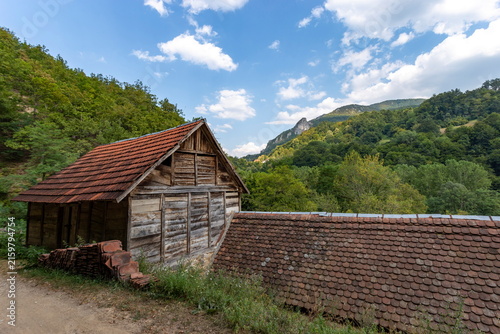 Wooden Barn and Country Road in Mountainous Landscape on Sunny Summer Day