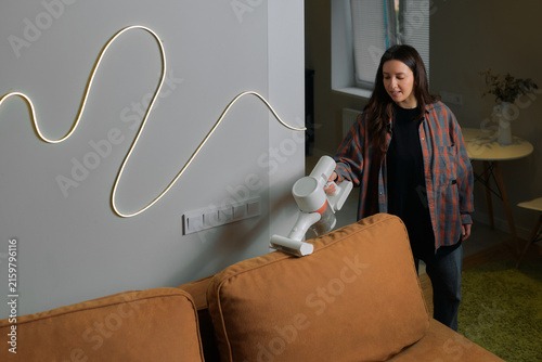 Konstfotografi Woman holds a cordless vacuum cleaner while cleaning a couch in a living room