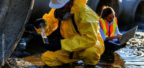  environmental scientists collecting water samples near large concrete industrial drainage pipes,