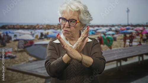 Foto Woman with hands crossed in front, palms out in a stop refusal gesture on a crowded street near a beach; defiance boundary