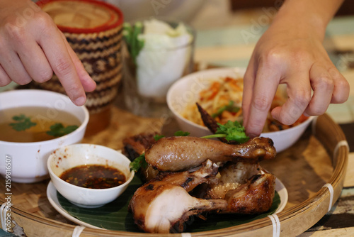 Fotografie Hands Reaching for Grilled Chicken and Traditional Thai Side Dishes