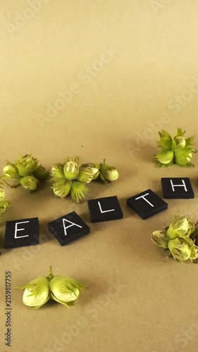 Slow camera gliding over the word 'healthy' spelled out in black letter tiles, surrounded by fresh, young, green hazelnuts on a smooth light brown paper background, emphasizing natural food