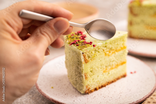 Pistachio green cake with cup of coffee with hand on brown concrete, close up, side view, selective focus