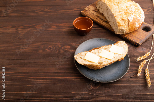 Slice of homemade bread with butter on plate on brown wooden, copy space, side view.