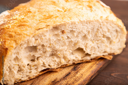 Slice of homemade bread with butter on plate on brown wooden, close up, side view, selective focus.