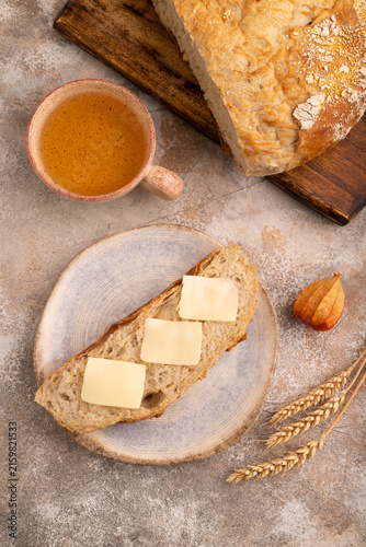 Slice of homemade bread with butter on plate on brown concrete, close up, top view.
