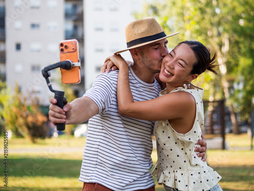 Young man and woman sharing a romantic moment while filming themselves with a mobile phone mounted on a handheld stabilizer.