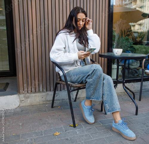 Nice woman sitting in street cafe using smartphone and drinking coffee