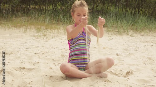 Little beautiful girl pours sand on shore of sea