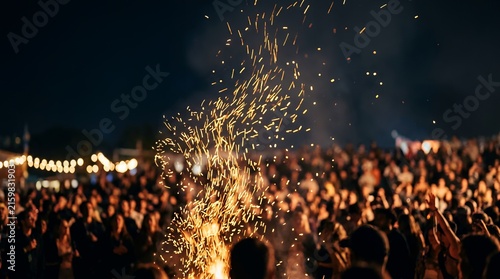 Golden sparks rising from a bonfire at a night music festival with a blurred crowd.
