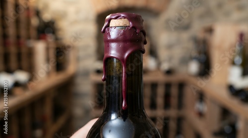 Macro view of burgundy wax seal dripping over a premium wine bottle neck in a cellar.