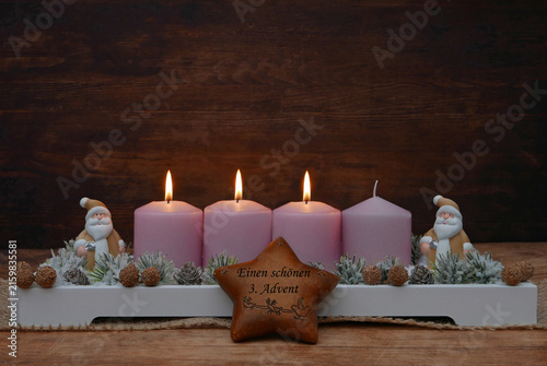 Einen schönen dritten Advent. Rustikales Gesteck dekoriert mit Weihnachtsmann Figuren, Stern und Tannenzweigen vor einem rustikalem Holzhintergrund mit Platz für Text.