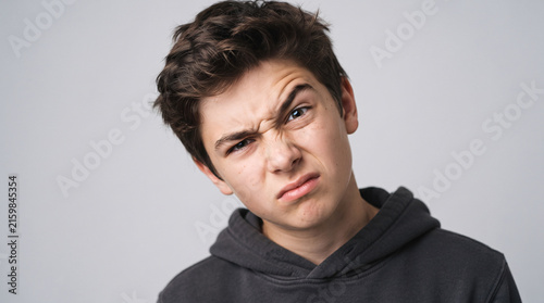 Portrait of displeased or skeptical teenage boy making a grimace on grey background