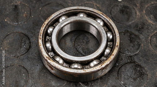Used automotive metal ball bearing with light rust and grease on a black textured rubber mat