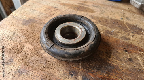 Worn automotive rubber suspension bushing with deep cracks and metal sleeve on wooden workbench