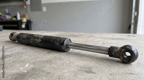 Used, worn automotive lift support lying on a light-colored workbench in a garage