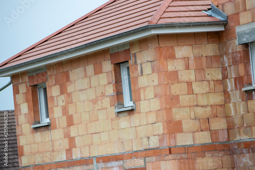 Une maison individuelle en cours de construction, réalisée en briques alvéolaires, avec une toiture en tuiles terre cuite et des menuiseries extérieures déjà posées.