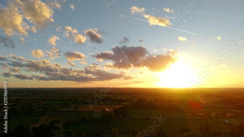 Evening sunlight over countryside fields and rural villages. Golden hour sky filled with dramatic clouds above farmland horizon. Warm sunset glow illuminating agricultural landscape across open