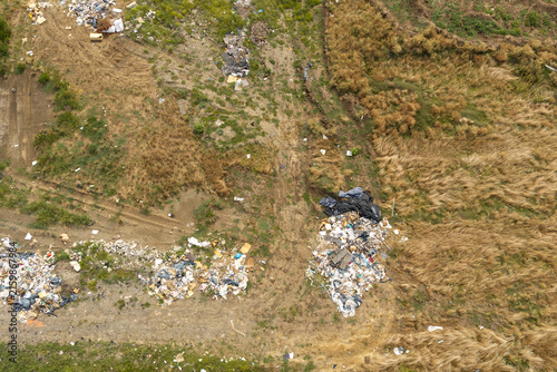 Aerial top down view of illegal garbage dumping and construction waste scattered across dry grassland, highlighting environmental pollution and land degradation under bright daylight.