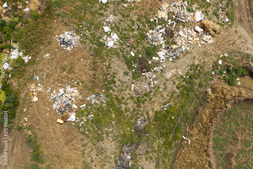 Top down aerial view of illegal trash and plastic waste dumped on open green fields and soil under bright daylight, highlighting environmental pollution and ecological damage issues.