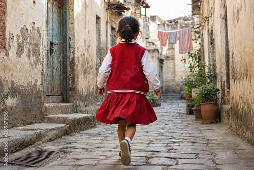 Little girl in red and white uniform walking in a traditional Indonesian village alley