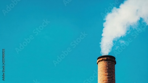 Brick chimney emitting white smoke against a clear blue sky