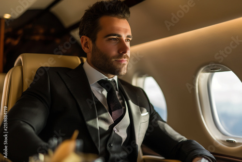 Wealthy businessman in a three-piece suit looking out the window inside a private jet cabin