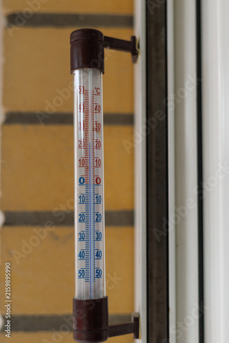 Old analog outdoor thermometer mounted beside a residential window for monitoring air temperature. Concept of traditional temperature measurement, weather observation and everyday household equipment.