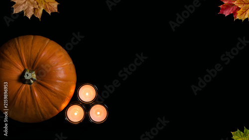 Autumn pumpkin with glowing candles and fall leaves on black background for seasonal decor
