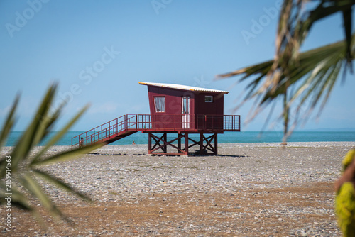 Fotografie Red wooden lifeguard hut with stairs standing alone on a deserted pebble beach u