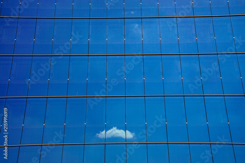 Modern blue glass building facade with a small white cloud reflected across geometric panels, creating a clean architectural background for business, technology and design projects.