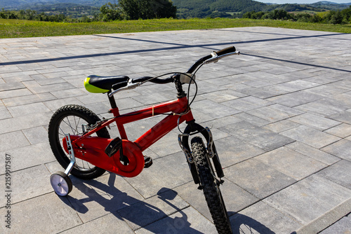 Kids bike with a black seat and sturdy training wheels for stability in front of a home garden
