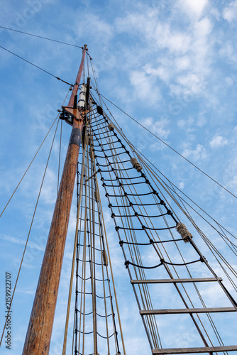 Canvastavla Wooden mast of a vintage sailboat with a rope ladder and complex rigging against a blue sky with clouds