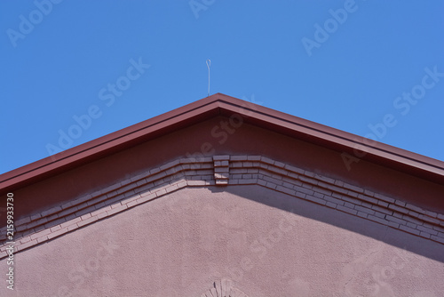 Canvastavla A building triangular gable roof with a single thin metal lightning rod wire mounted on the top ridge against a clear blue sky