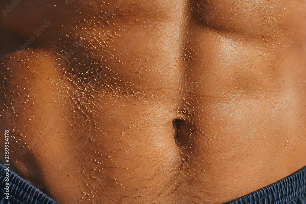 Fototapeta premium Tanned Male Torso with Water Drops and Sand at the Beach