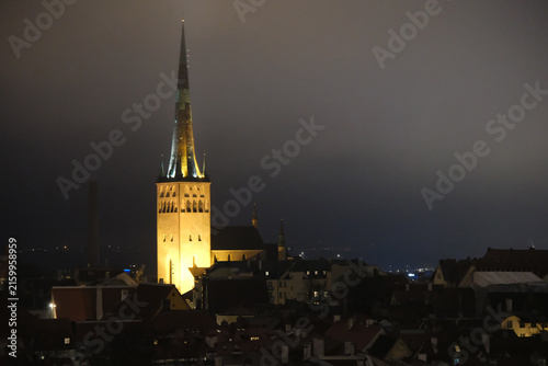 St. Olaf's Church illuminated at night, with its Gothic spire rising above the rooftops of Tallinn Old Town.