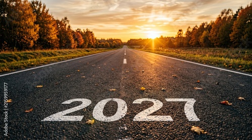 Autumn highway at sunset displaying 2027 painted on asphalt with trees with painted surface during paved road 2027 perspective transition landscape pavement distance roadside outdoors concept with new