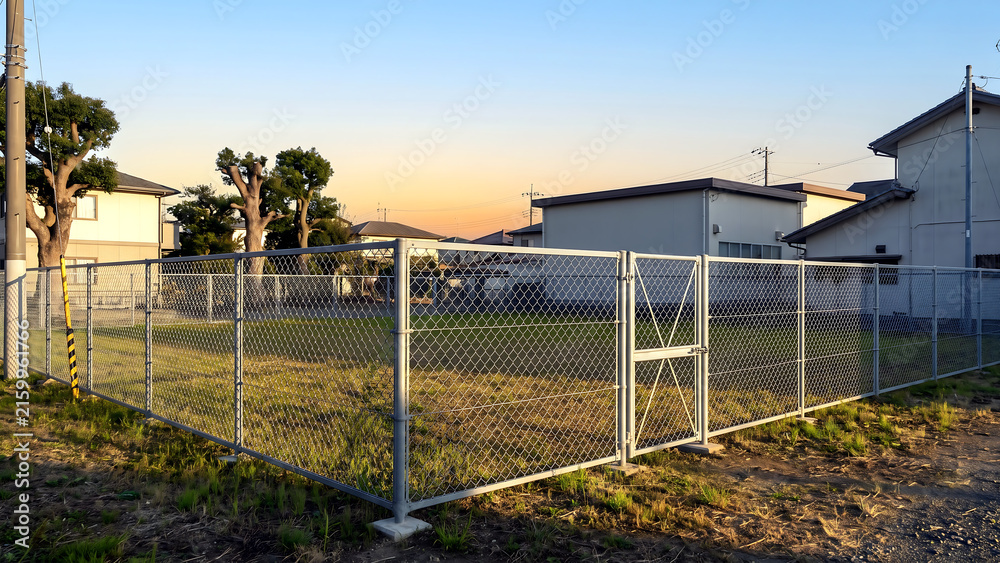 Fototapeta premium 夕焼け空の下金網フェンスと門扉に囲まれた空き地