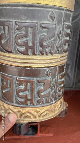 Vertical footage of a traditional Buddhist prayer wheel decorated with the sacred Om Mani Padme Hum mantra and ornamental Buddhist artwork. The close-up captures the detailed religious craftsmanship