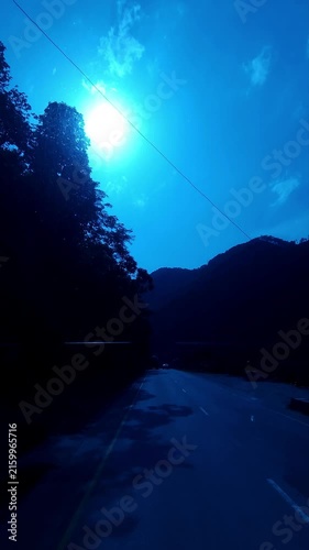 Vertical Mountain Road at Sunset with Bright Sun and Blue Sky  Scenic Himalayan Hill Landscape  Silhouette of Trees and Mountains  Peaceful Road Journey  Travel and Nature Background