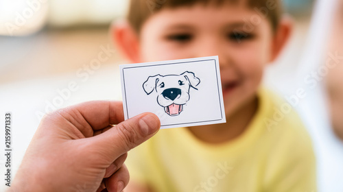A child holds a card with an illustration of a dog to show his mouth to a the...