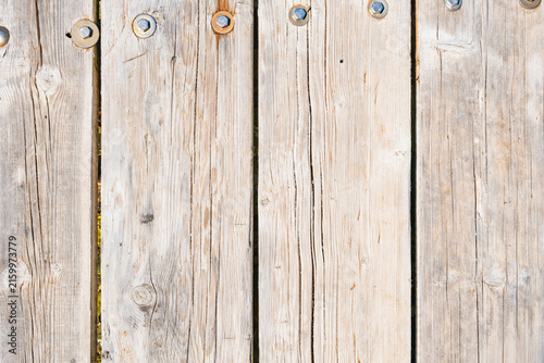 Close view of weathered pale wooden planks joined with large metal bolts and washers, showing grain, knots, cracks, and narrow gaps