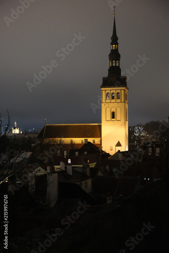 illuminated St. Nicholas Church towering over the historic old town buildings at night