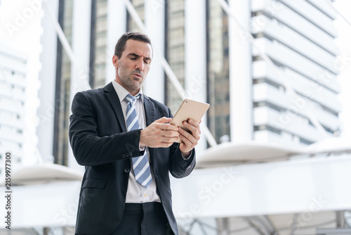Foto An uncomfortable overworked businessman looking at tablet while walking outside