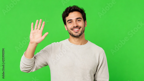 A smiling young man waves hello against a vibrant green background, exuding friendliness and approachability.