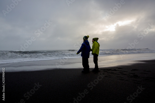 Children running from and to the ocean in black sand beach of Reynisfjara and the mount Reynisfjall in Iceland on a cold rainy day
