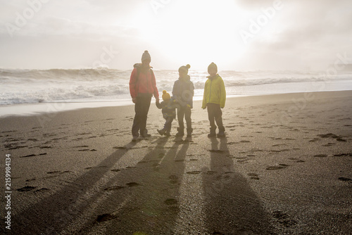 Family posing against the sun in black sand beach of Reynisfjara and the mount Reynisfjall in Iceland